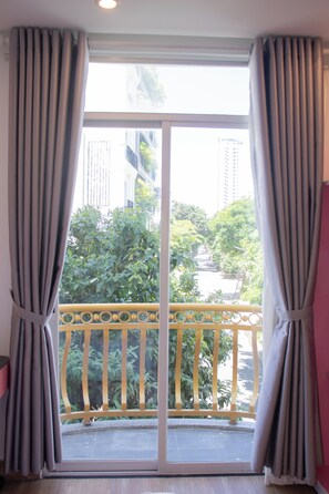 Une pièce dotée d’une grande porte-fenêtre coulissante qui donne sur un balcon avec une rambarde jaune et de la verdure à l’extérieur.