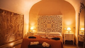 A hotel room with an arched doorway, a bed with a swan-shaped pillow, two bedside lamps, and a large mirror.