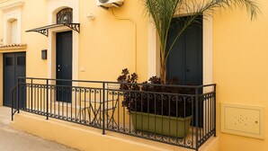 A yellow building with a black door, a window with a metal grill, a potted plant, and an air conditioning unit.