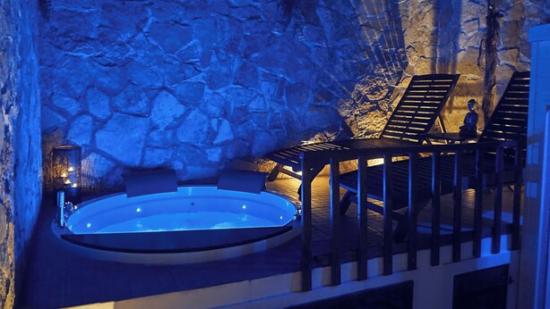 A hot tub with a stone wall backdrop, a seating area with a railing, and a statue.