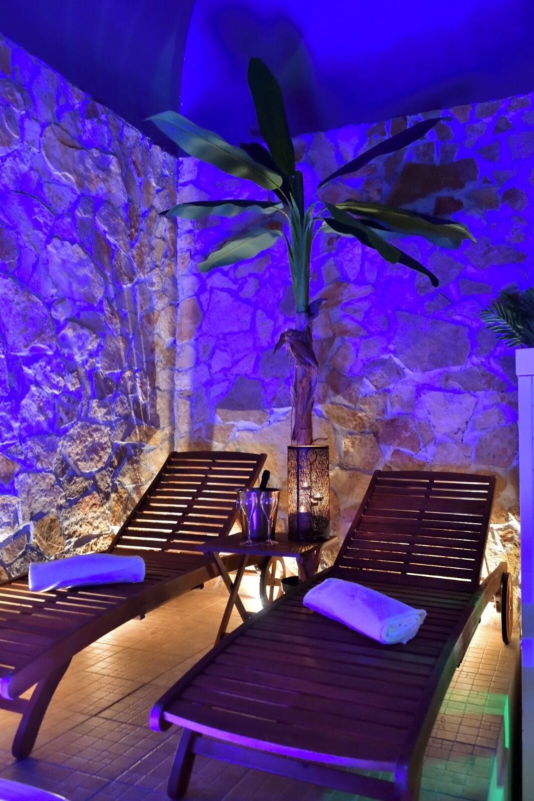 A spa area with wooden loungers, a stone wall, and a large plant.