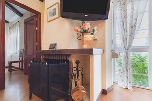 Quarto com lareira, televisão fixada acima e janela com cortinas, além de porta que dá acesso a outro cômodo.