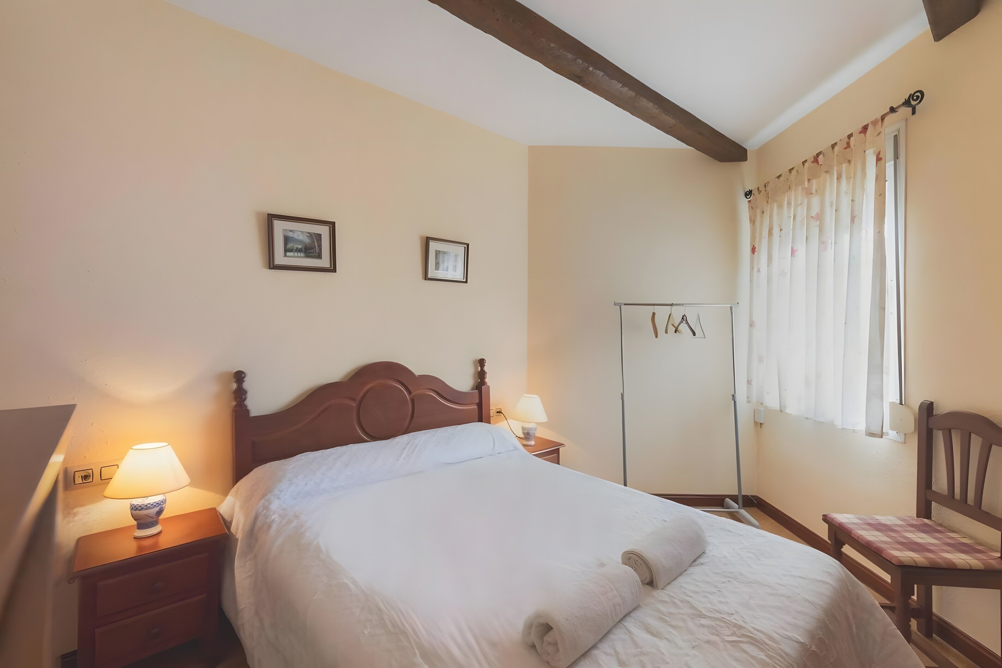 Una camera d'albergo con un letto in legno, due lampade sui comodini, un armadio e una sedia.