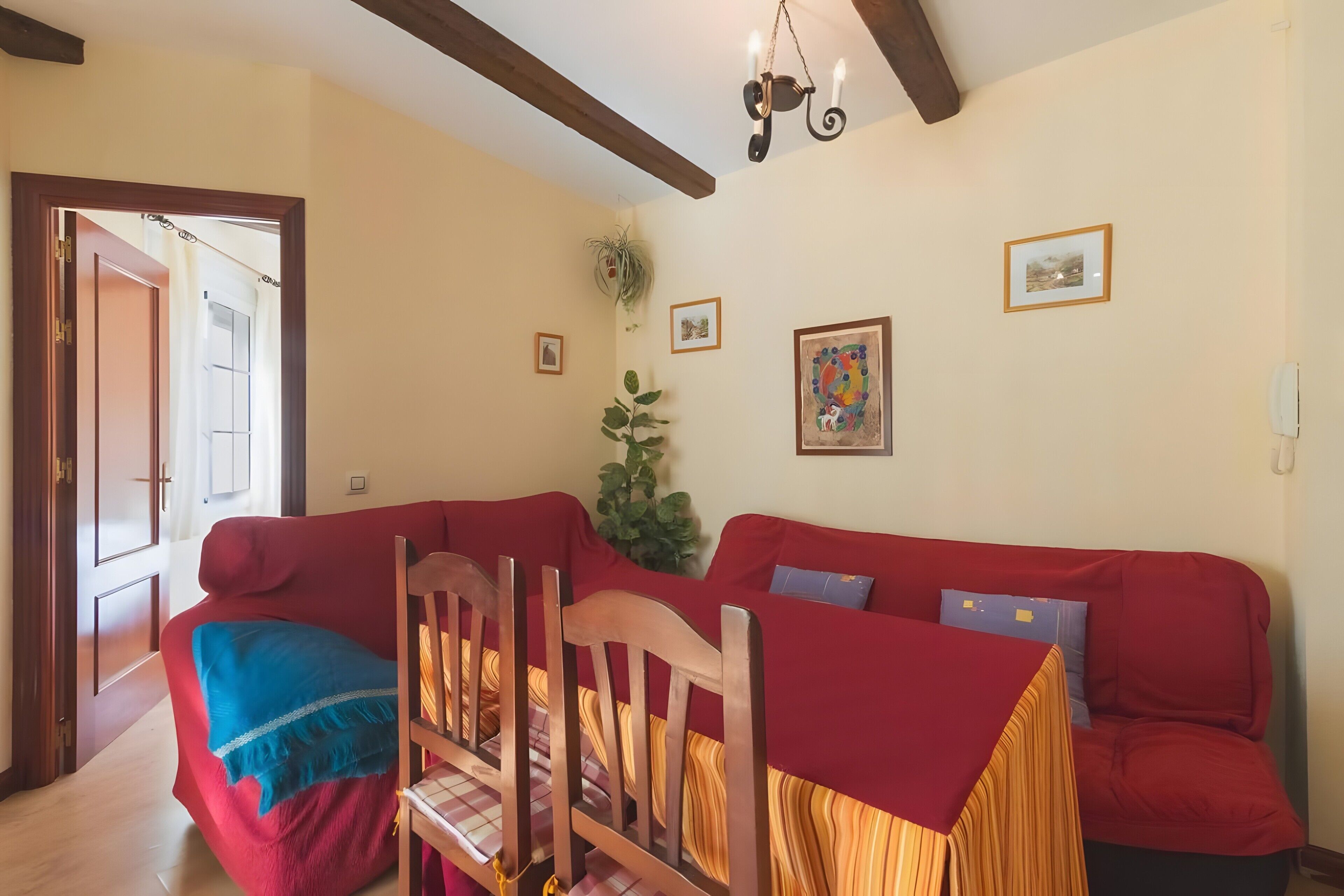 Ein rotes Sofa, Holzsessel, eine Chandelüster und gerahmte Bilder an der Wand.