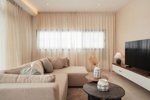 Un salon moderne avec un canapé, une table basse, un téléviseur et une fenêtre avec des rideaux.