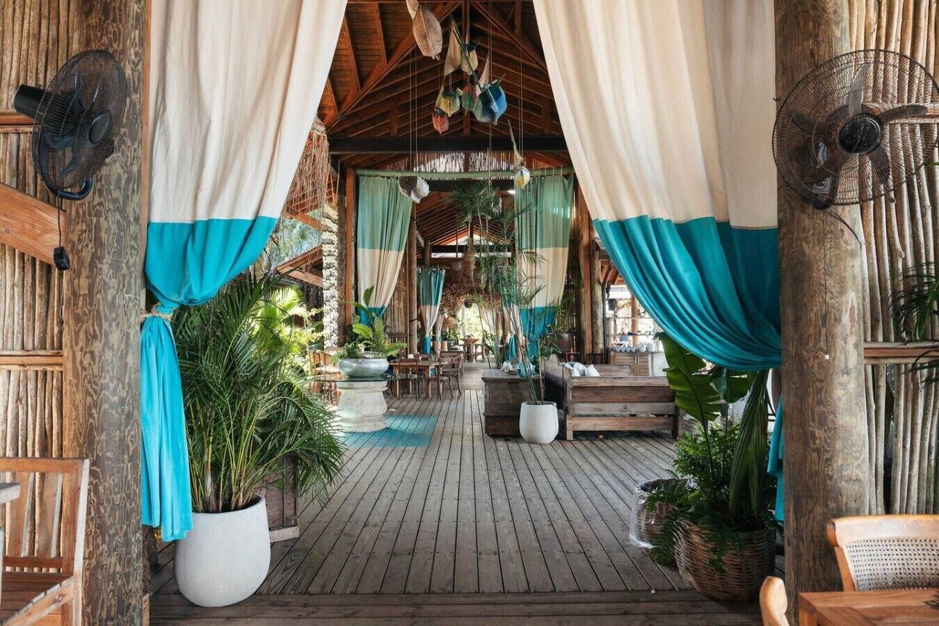 A wooden deck with a thatched roof, potted plants, and a seating area with a table and chairs.