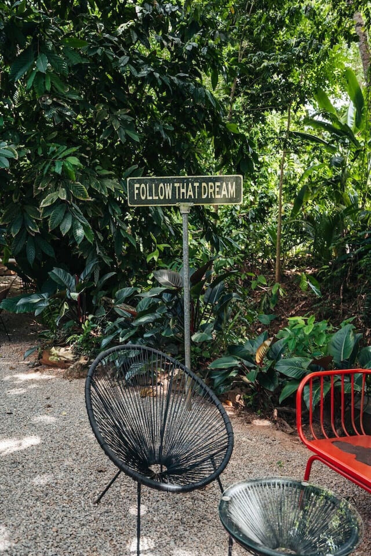 A garden with a motivational sign, a metal chair, and a red bench.