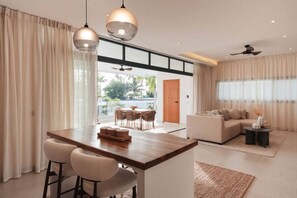 Un salon moderne comprenant un canapé, un coin repas avec une table et des chaises, et un espace cuisine avec un comptoir et des tabourets.