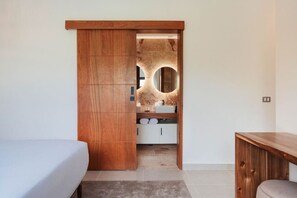 Ein Schlafzimmer mit Holzschrank, Bett, Nachttisch und angrenzendem Badezimmer, das durch einen Bogen sichtbar ist.
