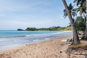 Uma praia com águas cristalinas, palmeiras e uma ilha ao longe.