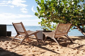 Two wicker lounge chairs on a sandy beach with a view of the sea and a tree with green leaves. - 2BR Oceanfront • Steps to Beach • Sol de Arena B6 (Las Terrenas)
