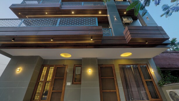 A multi-story building with wooden balconies, recessed lighting, and large windows. - Alaya Stays Zinnia 2BHK Apartment (Greater Noida)