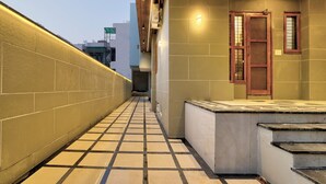A corridor with tiled flooring, a wooden door, and a small window. - Alaya Stays Zinnia 2BHK Apartment (Greater Noida)