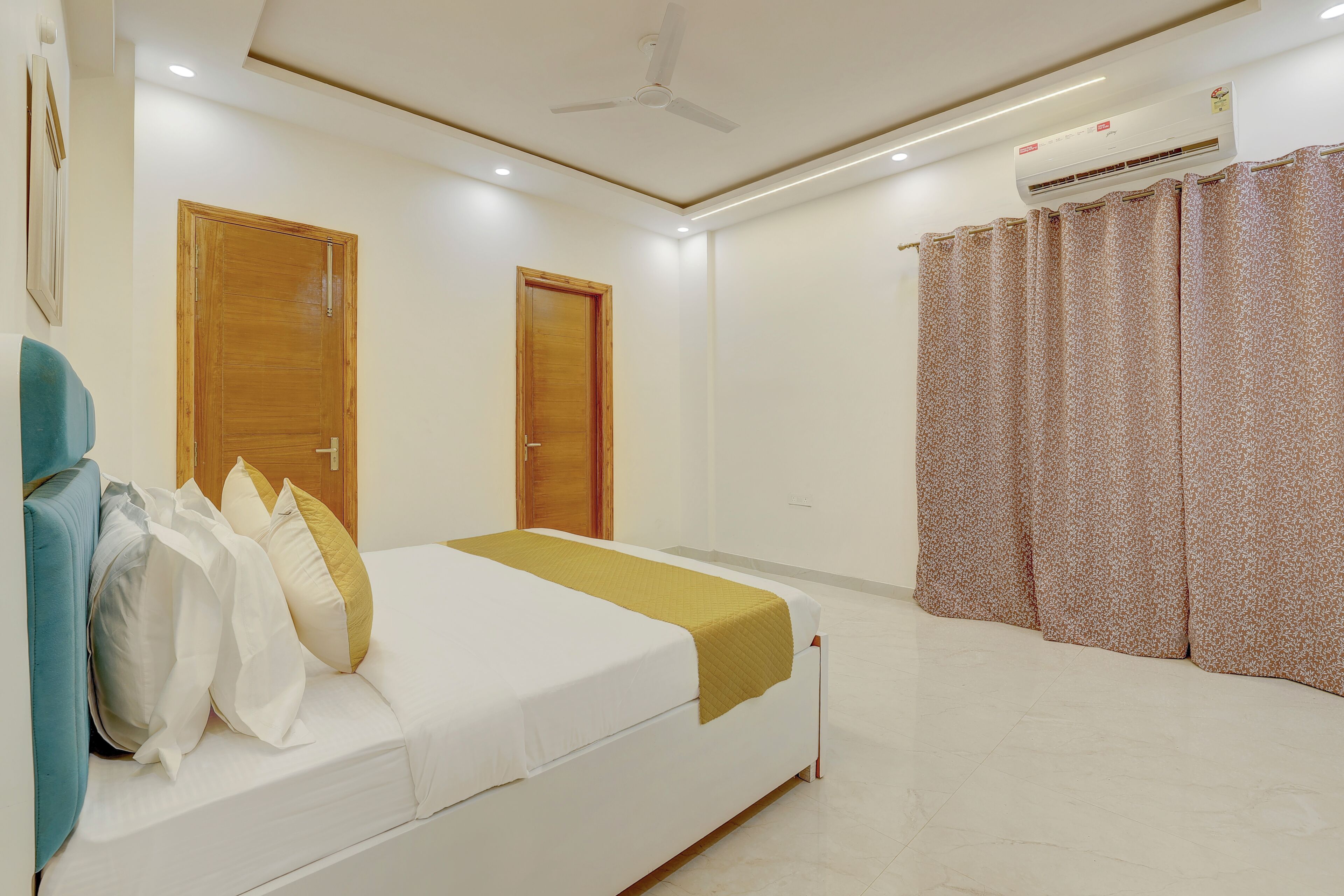 A hotel room with a bed, a ceiling fan, an air conditioning unit, and a window with curtains.