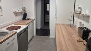 Een moderne keuken met een vaatwasser, koffiezetapparaat en broodrooster. Er is een houten aanrecht en een klein plankje met keukengerei.