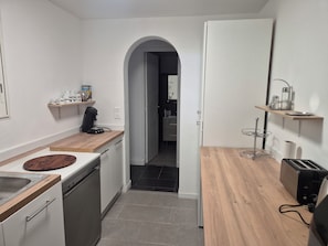 Eine moderne Küche mit Geschirrspüler, Kaffeemaschine und Toaster. Es gibt eine Holzarbeitsplatte und eine kleine Ablage mit Küchenutensilien.