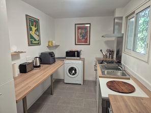 Eine kleine Küche mit Waschmaschine, Mikrowelle, Toaster und Spüle inklusive Geschirrgestell.