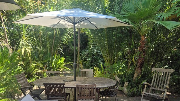 Een terras buiten met rieten meubels, een ronde tafel en een parasol.