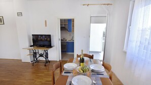 Et spiseområde med et bord dækket til to personer, et fjernsyn og et køkken i baggrunden.