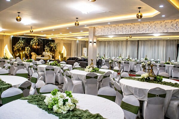 Un salón de banquetes con mesas redondas, manteles blancos y cintas verdes.