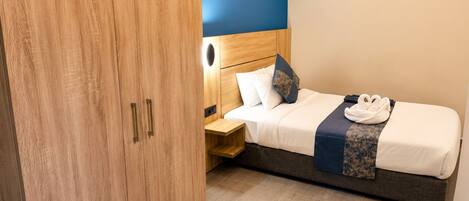 Habitación de hotel con un armario de madera, una cama con cabecero, una mesita de noche y una toalla sobre la cama.