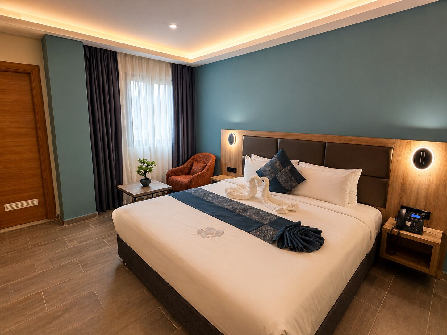 Habitación de hotel con una cama grande, cabecera de madera, una mesita con una planta y una silla.