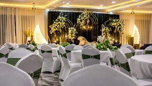 Une salle de banquet avec des rangées de tables et de chaises blanches, chacune agrémentée d’un ruban vert sur le dossier.