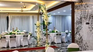 Une salle de banquet avec des tables rondes, des chaises blanches ornées de rubans verts et une arche florale décorative.