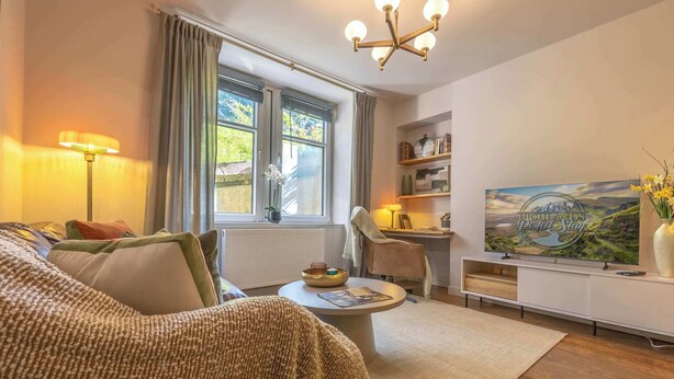 A cozy living room with a sofa, a coffee table, a lamp, a TV, and a bookshelf. - Cosy City Centre Flat | Summer Retreat | Sleeps 2 (Inverness)