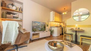 A modern living room with a sofa, a coffee table, a TV, and a kitchen area in the background. - Cosy City Centre Flat | Summer Retreat | Sleeps 2 (Inverness)