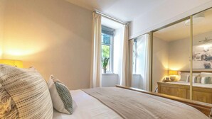 A bedroom with a large bed, a bedside table with a lamp, a window with curtains, and a mirror. - Cosy City Centre Flat | Summer Retreat | Sleeps 2 (Inverness)