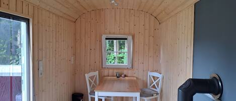 Interior de una cabaña de madera con una mesa, sillas, una ventana y una parrilla.
