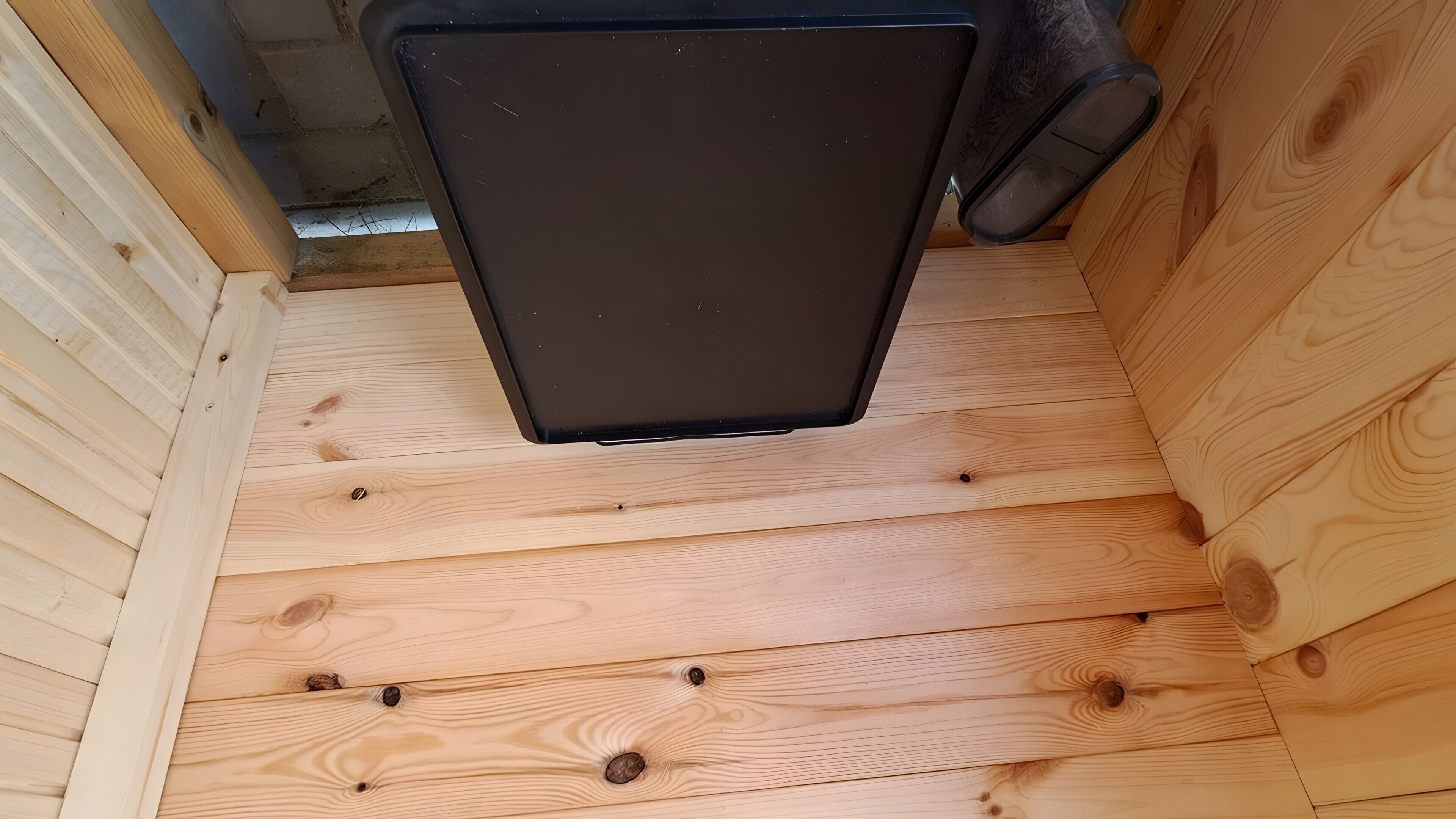 Una estructura de madera con un objeto negro encima, posiblemente una rejilla de ventilación, y un pequeño agujero en la pared.