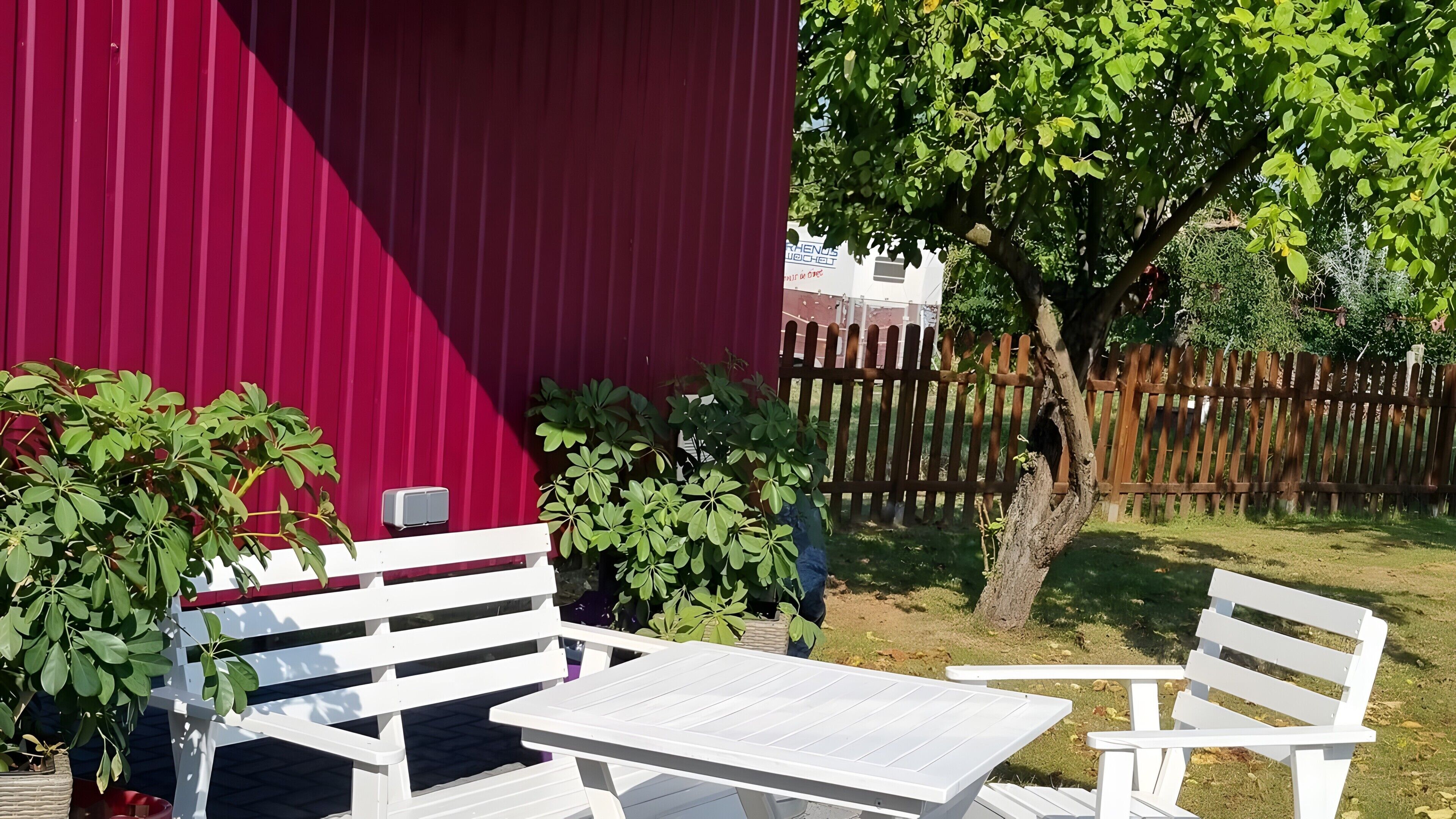 En uteplats med vita möbler, en röd byggnad och ett trästaket.