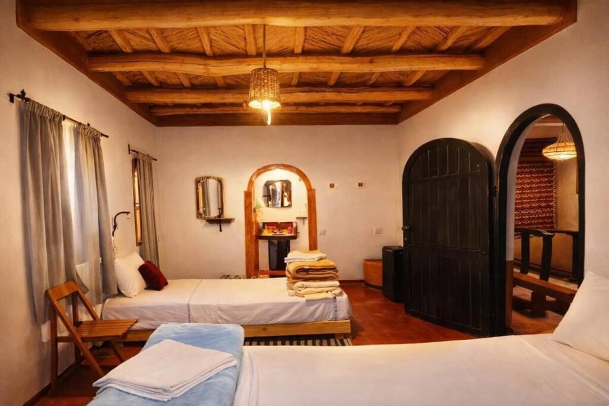Una habitación con dos camas, techo de madera, un espejo y una puerta.