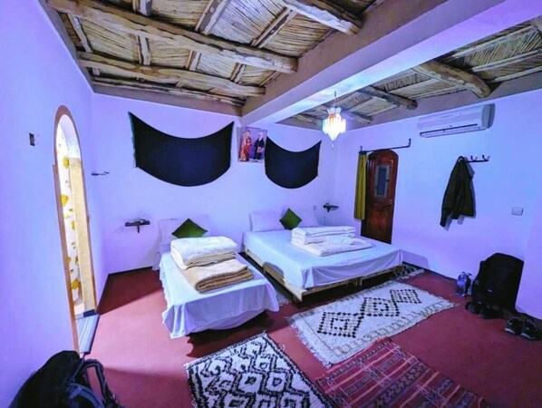 A room with two beds, a chandelier, a wooden ceiling, and a patterned rug.