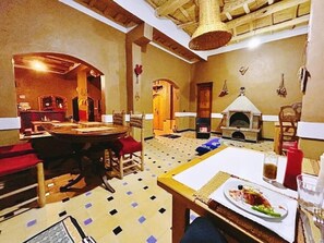 A dining area with a round table, chairs, a fireplace, and a patterned floor. - Riad Pizzeria Marhaba (Ait Sedrate Jbel El Soufla)