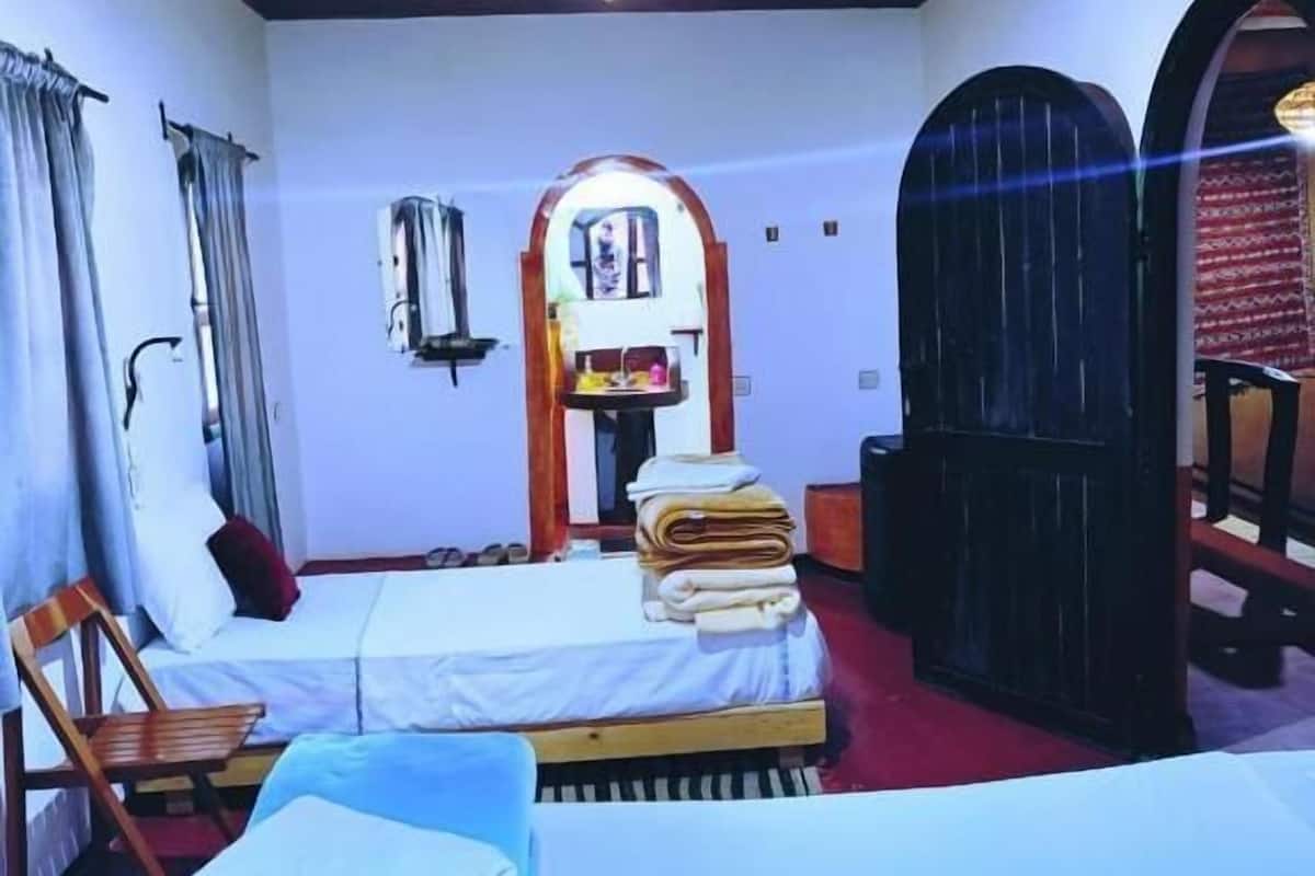 Una habitación con dos camas, techo de madera, una mesita con espejo y una puerta de diseño arqueado.