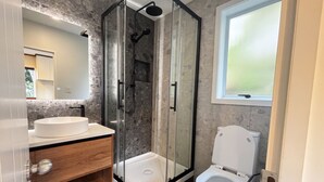 Ein modernes Badezimmer mit einer Duschkabine, einem weißen Waschbecken und einer Toilette.