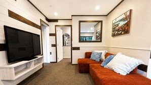 Ein modernes Wohnzimmer mit Flachbildfernseher, einer Couch mit Kissen, einem Spiegel und einem Gemälde an der Wand.