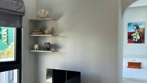Une chambre à coucher avec un lit, un téléviseur posé sur un meuble, une étagère avec des objets décoratifs et un tableau accroché au mur.