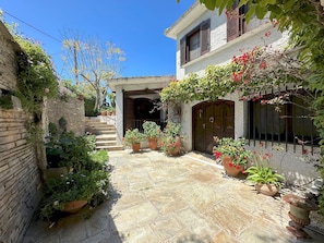 A courtyard with stone flooring, potted plants, a staircase, and a building with a wooden door.
