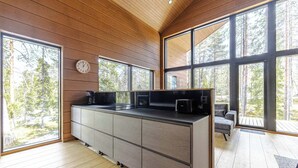 Una cocina moderna con una isla grande, techo de madera y ventanas amplias que dan a un bosque.