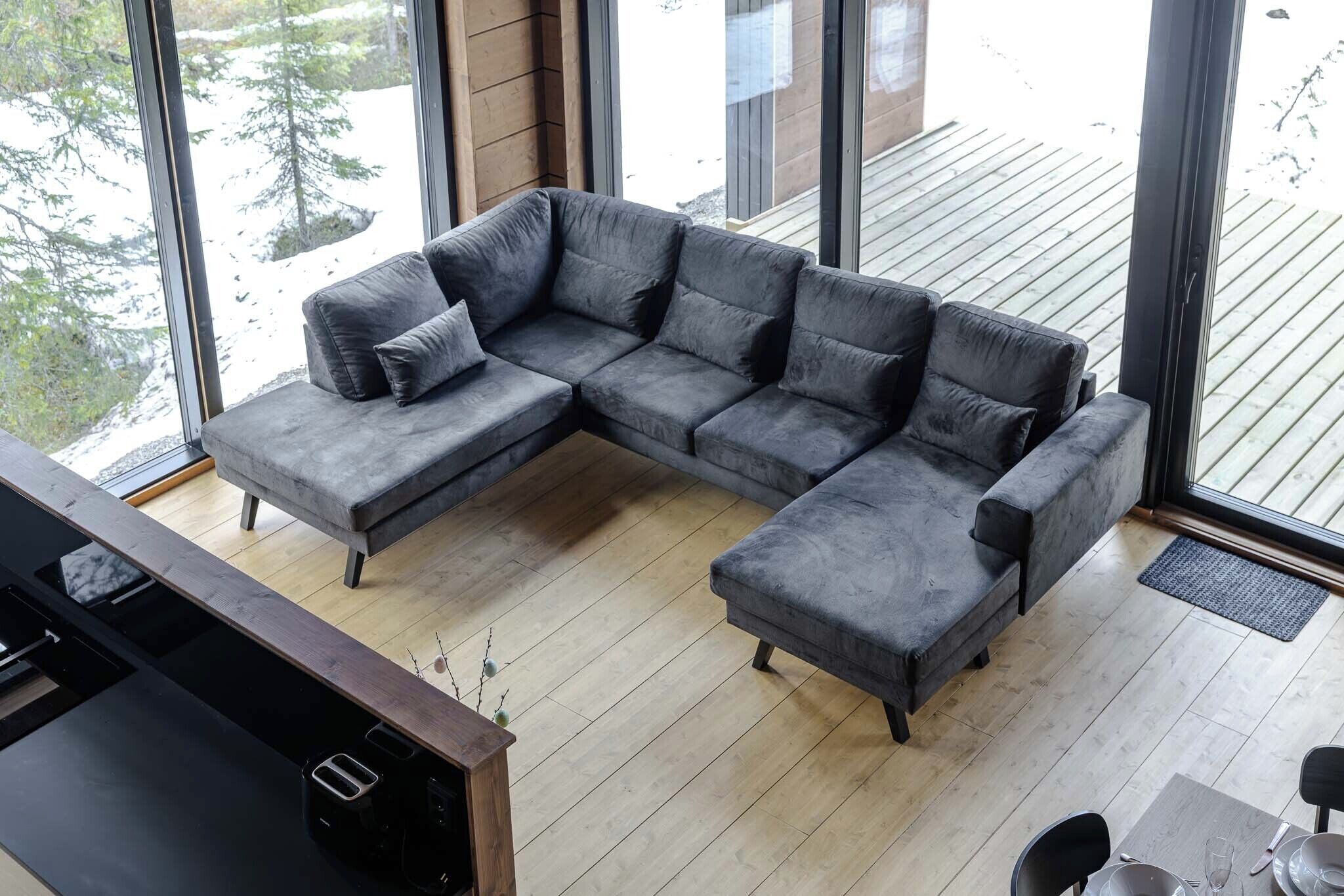 A modern living room with a sectional sofa, a dining table with chairs, and large windows offering a view of a snowy landscape.