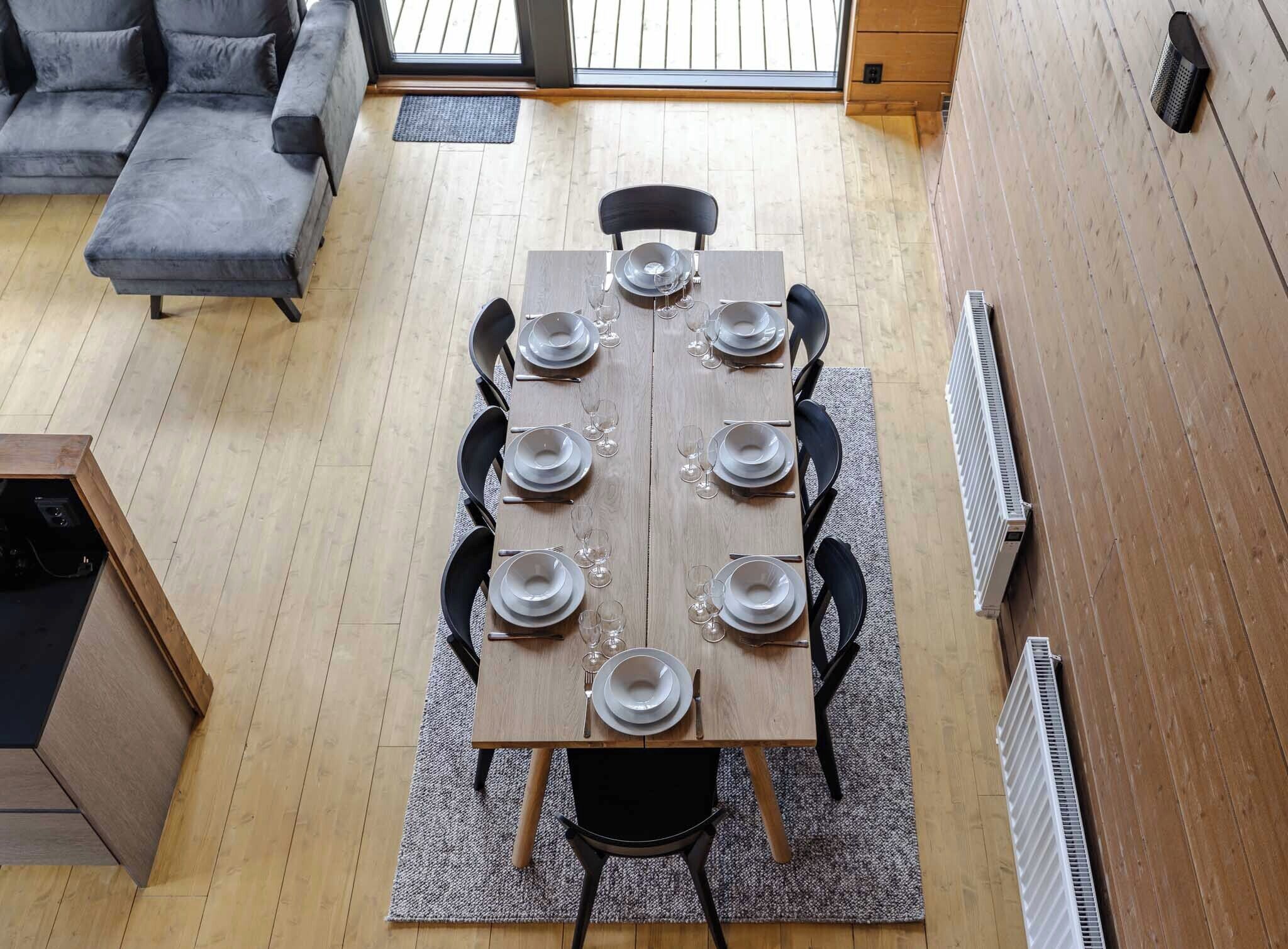 A dining area with a wooden table set for six, surrounded by black chairs.