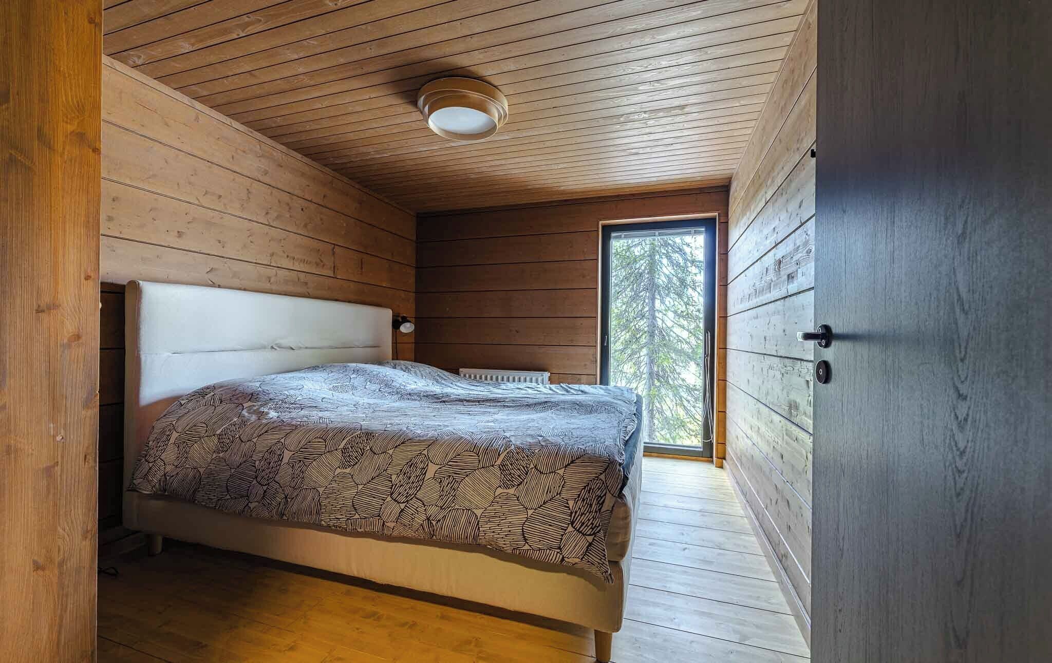 A bedroom with a bed, wooden walls, a window, and a ceiling light.
