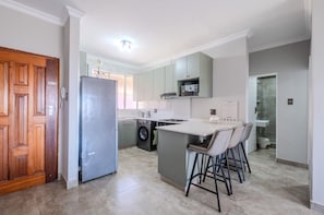 Una cocina moderna con lavadora integrada, una zona de bar con taburetes y un espacio de comedor independiente.