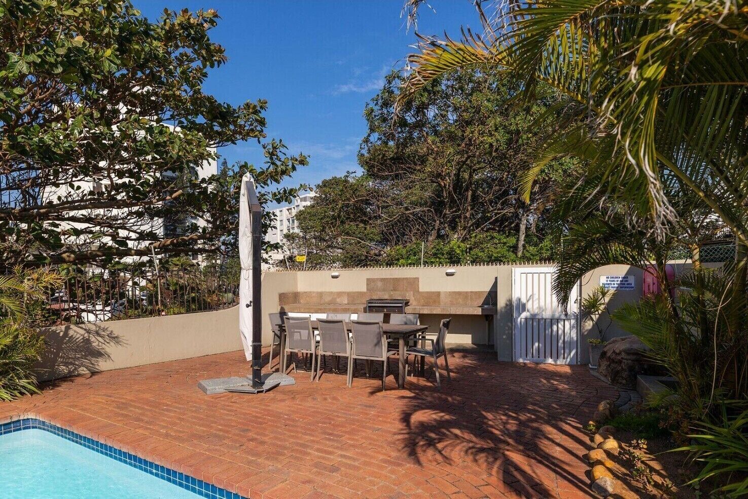 Un patio trasero con piscina, muebles de jardín, una parrilla de barbacoa y una valla blanca.