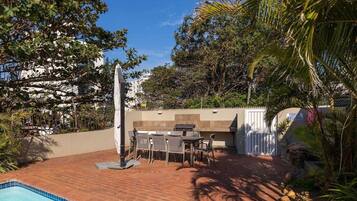 Un patio trasero con piscina, muebles de jardín, una parrilla de barbacoa y una valla blanca.