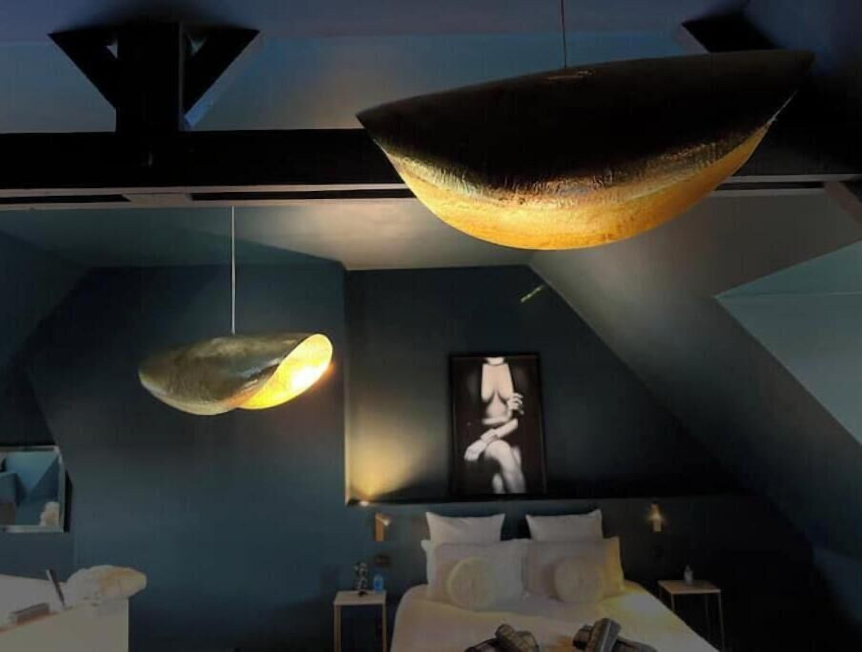 Et moderne hotelværelse med en seng, sengeborde, et billede på væggen og en anderledes pendellampe.